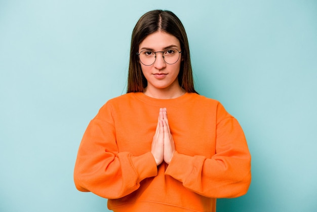 Young caucasian woman isolated on blue background praying showing devotion religious person looking for divine inspiration