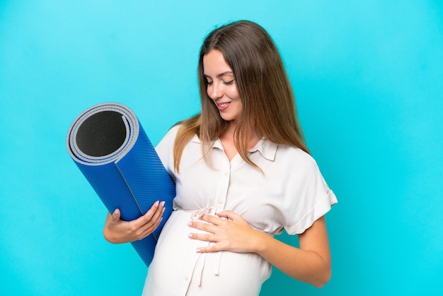 Young caucasian woman isolated on blue background pregnant and going to yoga classes