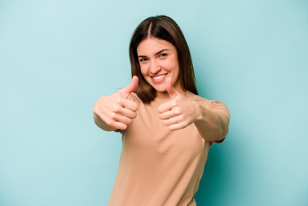 Young caucasian woman isolated on blue background raising both thumbs up smiling and confident