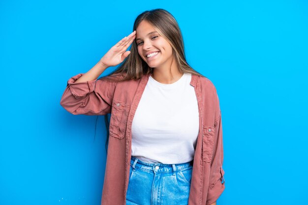 Young caucasian woman isolated on blue background saluting with hand with happy expression