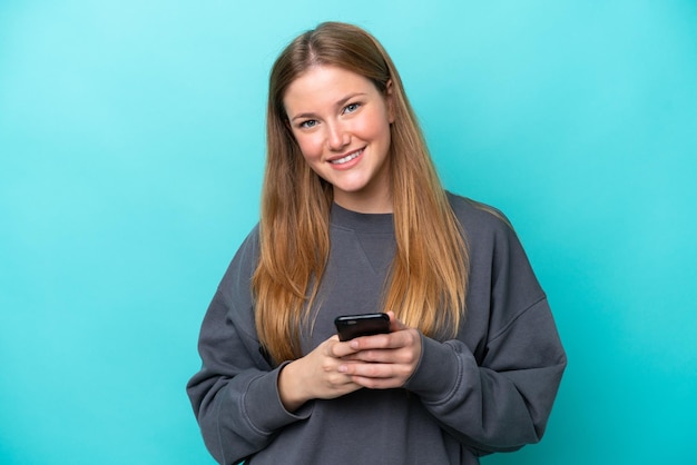 Young caucasian woman isolated on blue background sending a message with the mobile