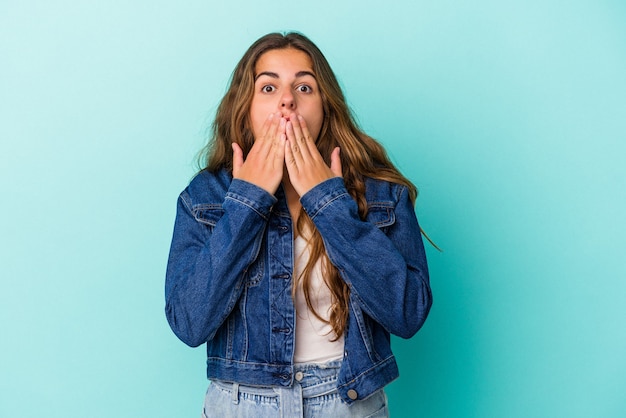 Young caucasian woman isolated on blue background  shocked, covering mouth with hands, anxious to discover something new.