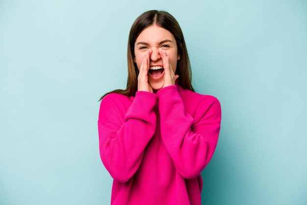 Young caucasian woman isolated on blue background shouting excited to front