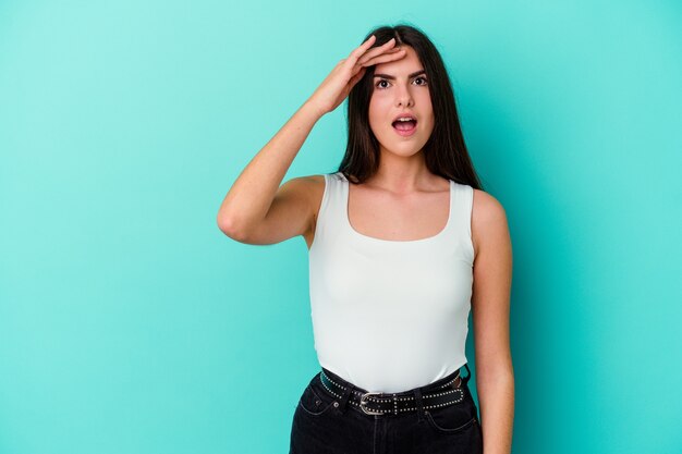 Young caucasian woman isolated on blue background shouts loud, keeps eyes opened and hands tense.