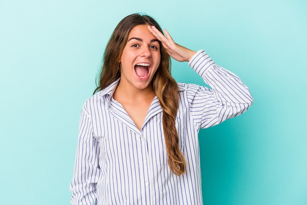 Young caucasian woman isolated on blue background  shouts loud, keeps eyes opened and hands tense.