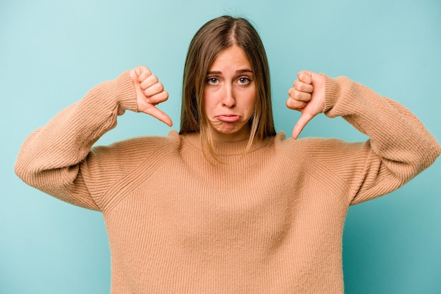 Young caucasian woman isolated on blue background showing a dislike gesture thumbs down Disagreement concept