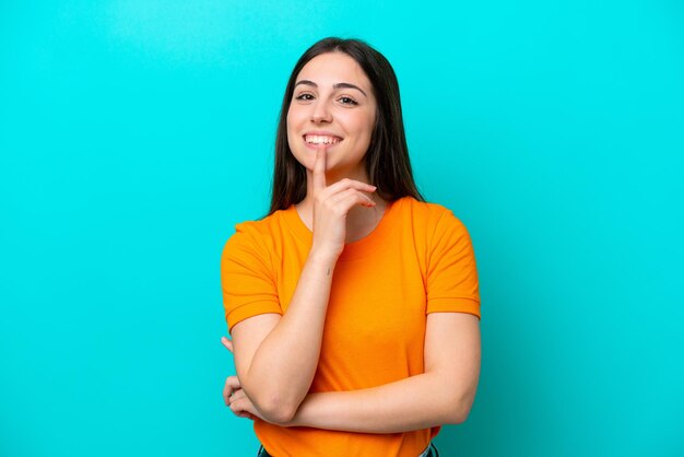 Young caucasian woman isolated on blue background showing a sign of silence gesture putting finger in mouth