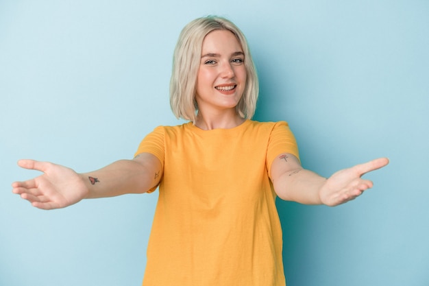 Young caucasian woman isolated on blue background showing a welcome expression.