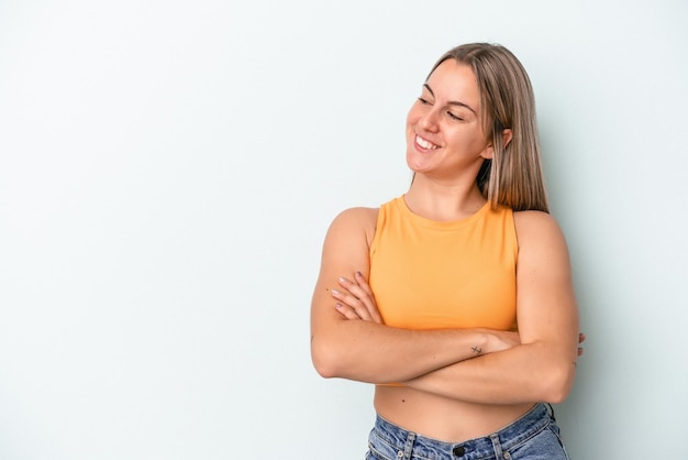 Young caucasian woman isolated on blue background smiling confident with crossed arms.