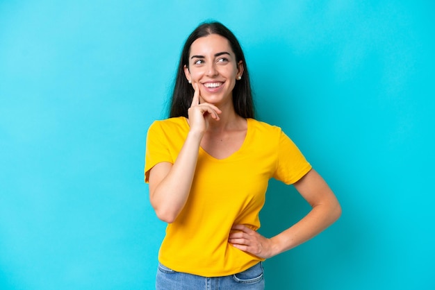 Young caucasian woman isolated on blue background thinking an idea while looking up