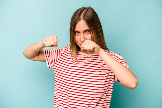 Young caucasian woman isolated on blue background throwing a punch anger fighting due to an argument boxing