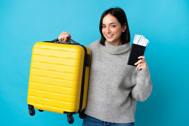 Young caucasian woman isolated on blue background in vacation with suitcase and passport