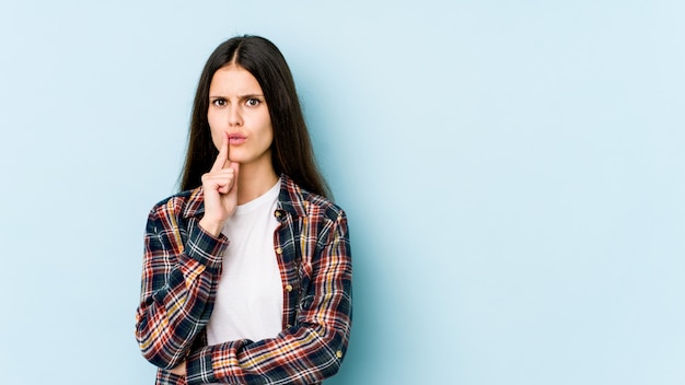 Young caucasian woman isolated on blue wall looking sideways with doubtful and skeptical expression.