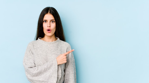 Young caucasian woman isolated on blue wall pointing to the side