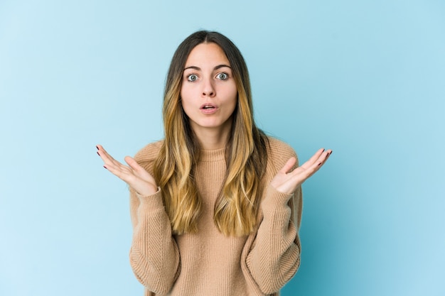 Young caucasian woman isolated on blue wall surprised and shocked.