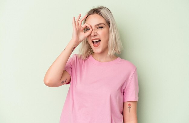 Young caucasian woman isolated on green background excited keeping ok gesture on eye.