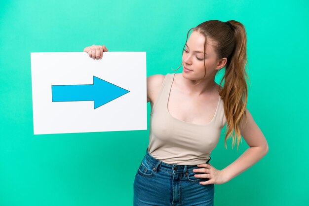 Young caucasian woman isolated on green background holding a placard with arrow symbol