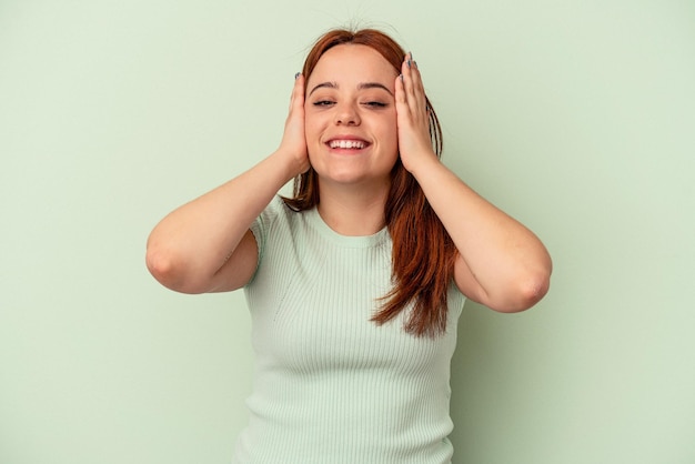 Young caucasian woman isolated on green background laughs joyfully keeping hands on head. Happiness concept.