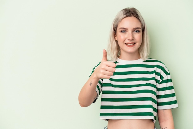 Young caucasian woman isolated on green background smiling and raising thumb up