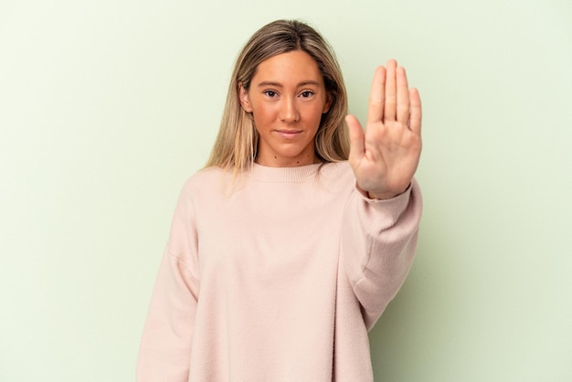 Young caucasian woman isolated on green background standing with outstretched hand showing stop sign, preventing you.