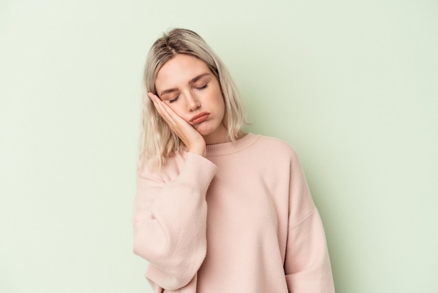 Young caucasian woman isolated on green background who is bored, fatigued and need a relax day.