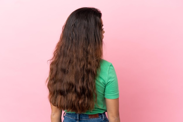 Young caucasian woman isolated on pink background in back position and looking side