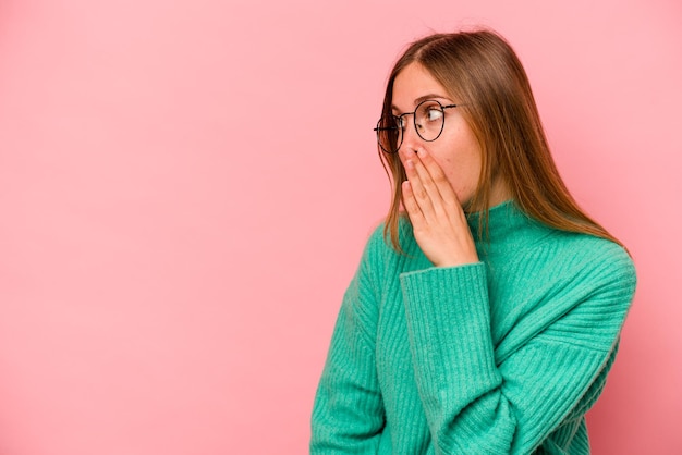 Young caucasian woman isolated on pink background being shocked because of something she has seen