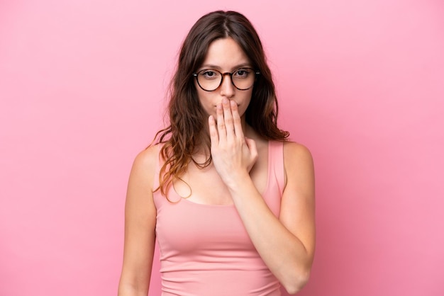 Young caucasian woman isolated on pink background covering mouth with hand