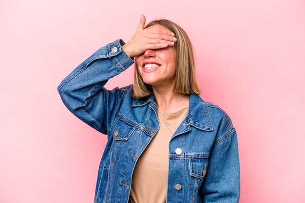 Young caucasian woman isolated on pink background covers eyes with hands smiles broadly waiting for a surprise