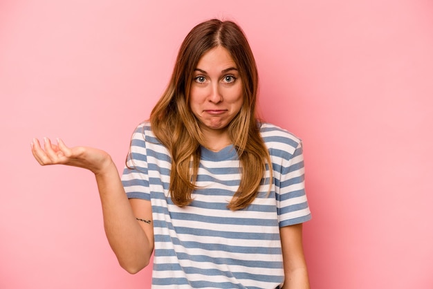 Young caucasian woman isolated on pink background doubting and shrugging shoulders in questioning gesture