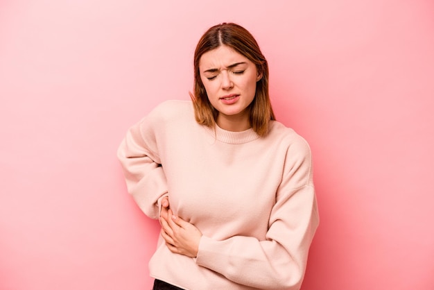 Young caucasian woman isolated on pink background having a liver pain stomach ache