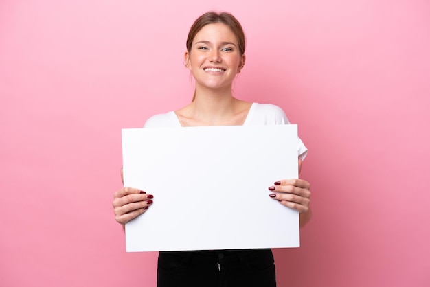 Young caucasian woman isolated on pink background holding an empty placard with happy expression