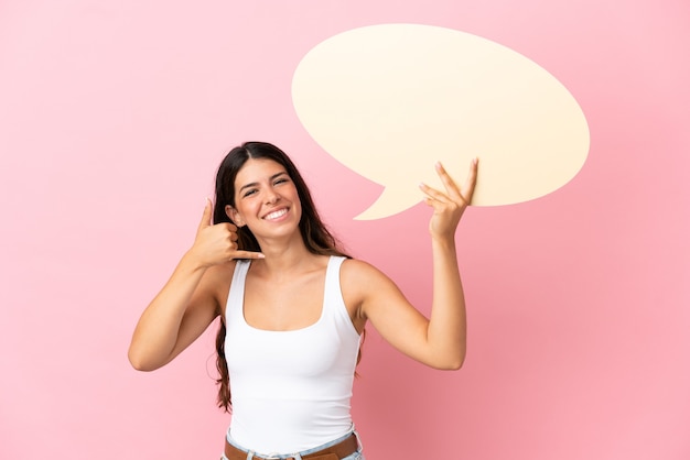 Young caucasian woman isolated on pink background holding an empty speech bubble and doing phone gesture