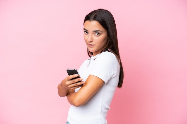 Young caucasian woman isolated on pink background holding a mobile phone and with arms crossed