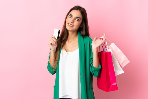 Young caucasian woman isolated on pink background holding shopping bags and a credit card