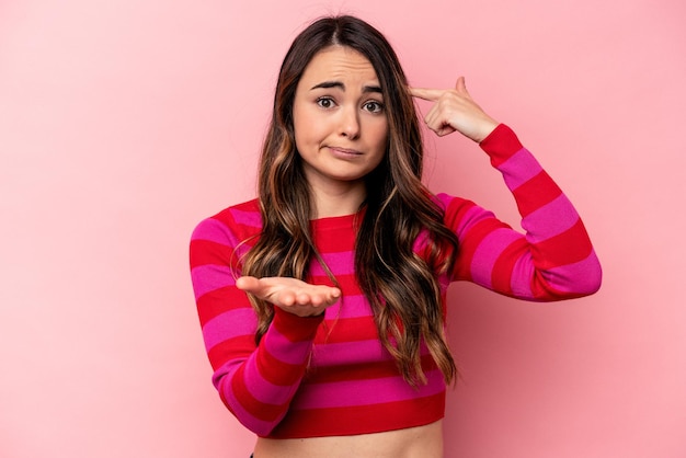 Young caucasian woman isolated on pink background holding and showing a product on hand