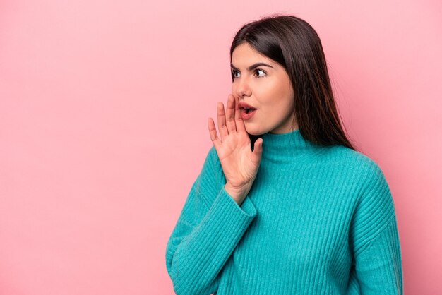 Young caucasian woman isolated on pink background is saying a secret hot braking news and looking aside