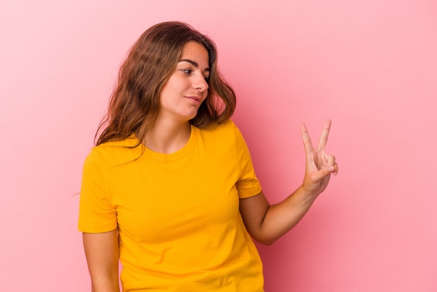 Young caucasian woman isolated on pink background  joyful and carefree showing a peace symbol with fingers.