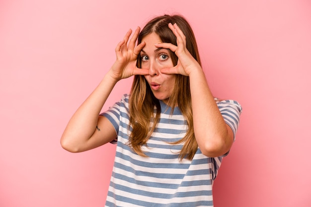 Young caucasian woman isolated on pink background keeping eyes opened to find a success opportunity