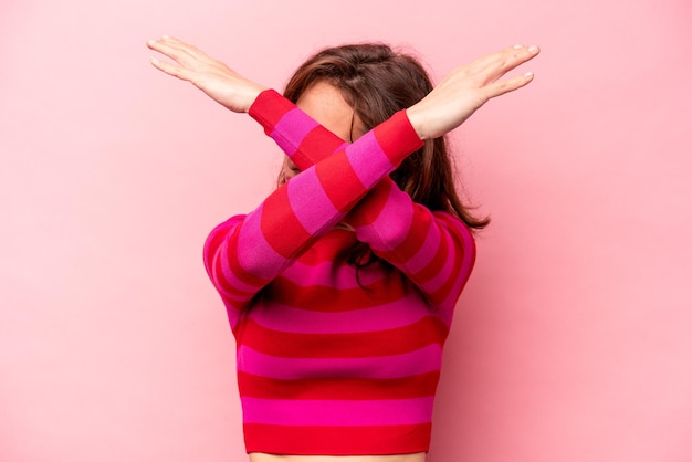 Young caucasian woman isolated on pink background keeping two arms crossed denial concept