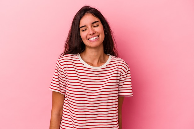 Young caucasian woman isolated on pink background laughs and closes eyes, feels relaxed and happy.