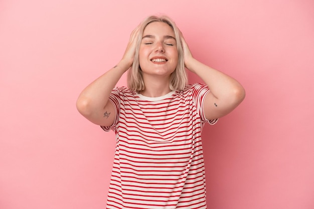 Young caucasian woman isolated on pink background laughs joyfully keeping hands on head. Happiness concept.