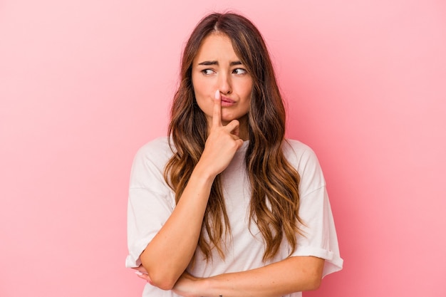 Young caucasian woman isolated on pink background looking sideways with doubtful and skeptical expression.