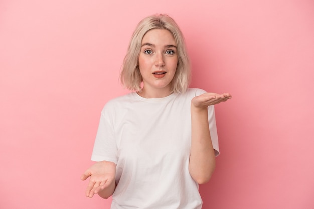 Young caucasian woman isolated on pink background makes scale with arms, feels happy and confident.