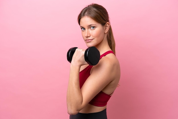 Young caucasian woman isolated on pink background making weightlifting