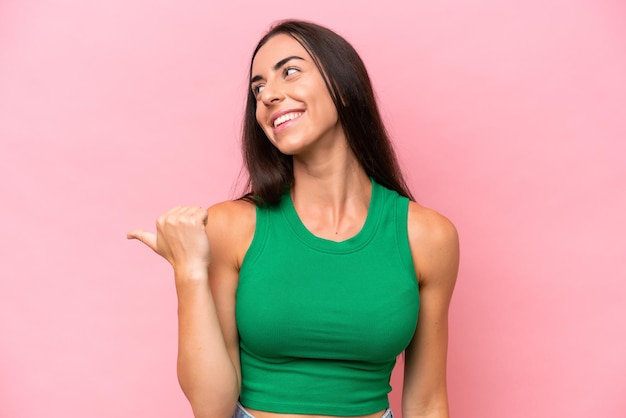 Young caucasian woman isolated on pink background pointing to the side to present a product