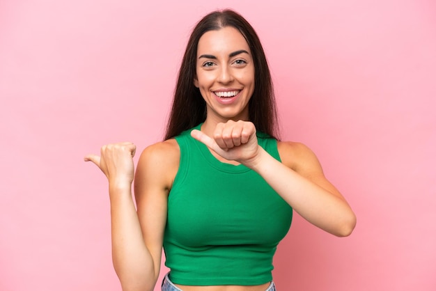 Young caucasian woman isolated on pink background pointing to the side to present a product