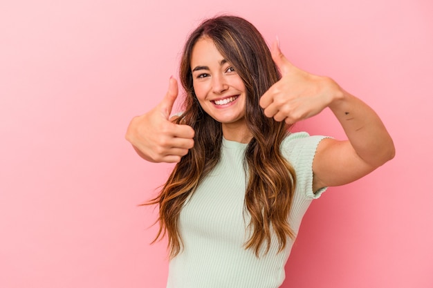 Young caucasian woman isolated on pink background raising both thumbs up, smiling and confident.