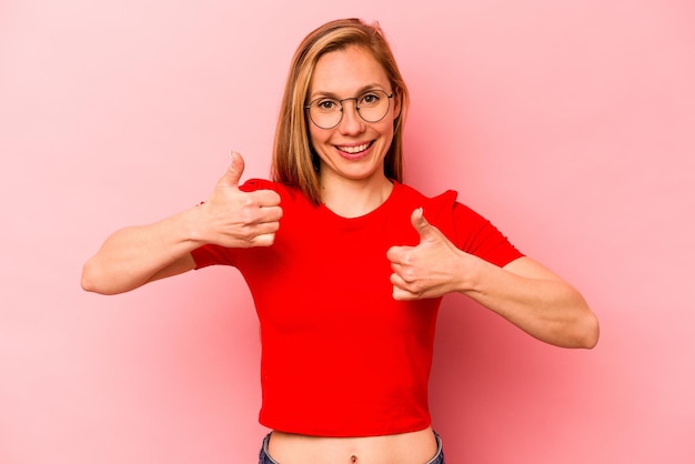 Photo young caucasian woman isolated on pink background raising both thumbs up smiling and confident