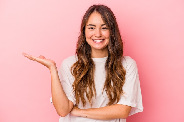 Young caucasian woman isolated on pink background showing a copy space on a palm and holding another hand on waist.